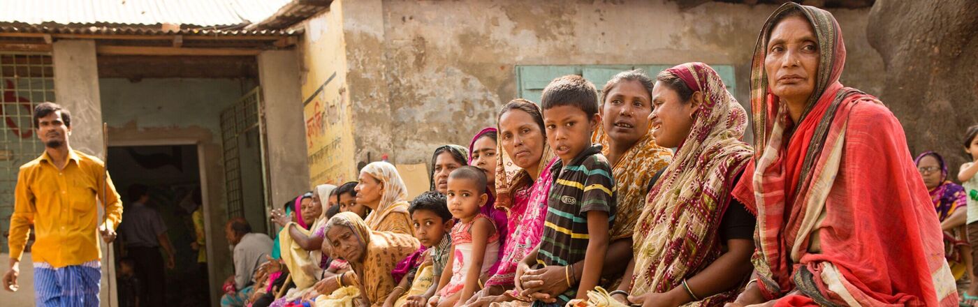 Ihr Unternehmen hilft mit einer Weihnachtsspende in 2024 Frauen und Kinder, die vor einem Gebäude auf ihre Sprechstunde bei den German Doctors in Indien warten