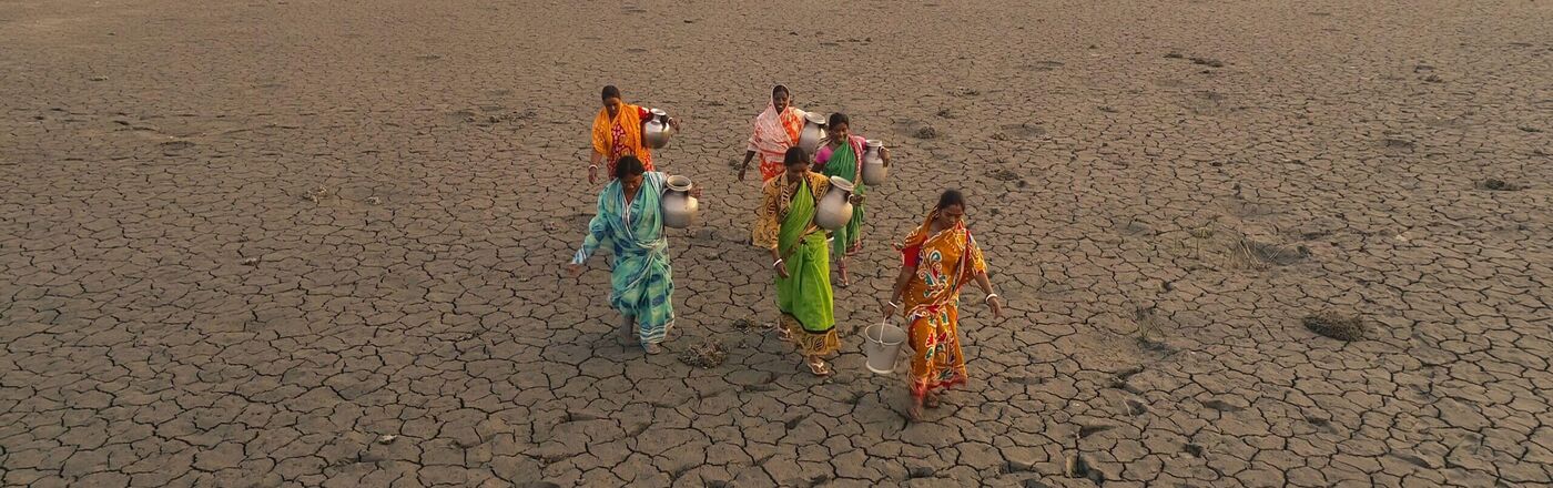 Frauen in Indien beim Wasserholen auf einem vertrockneten, rissigen Feld © ASHA